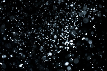 Blurry bokeh of falling white snow on black background