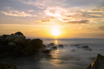 (Selective focus) Stunning long exposure picture of a rocky coast bathed by a smooth silky sea during a beautiful and dramatic sunset. Melasti Beach, South Bali, Indonesia.