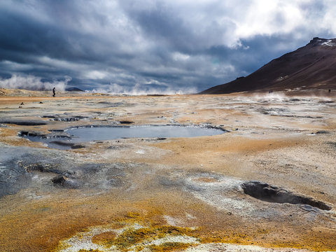 lonely person walking on Mudpots in the geothermal area Hverir, Iceland. The area around the boiling mud is multicolored and cracked.