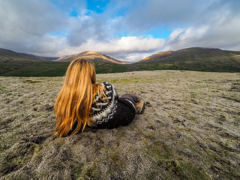 Scandinavian woman wearing traditionally patterned knitwear and lying on the mose, Iceland