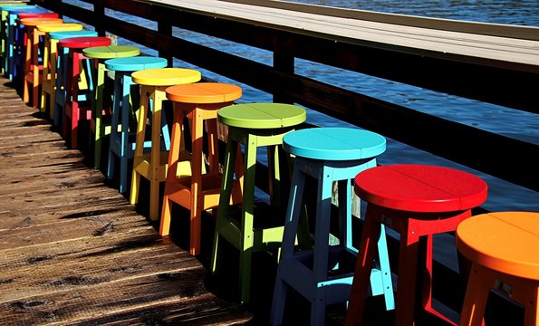Colored stools lined along the edhe of a warf that juts out into the Pacific Ocean