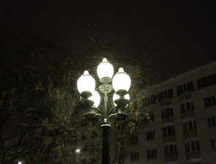 Pole with lanterns in the city on a winter night with snow and Blizzard.