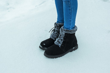 Women's feet in jeans and warm boots with fur on the snow.