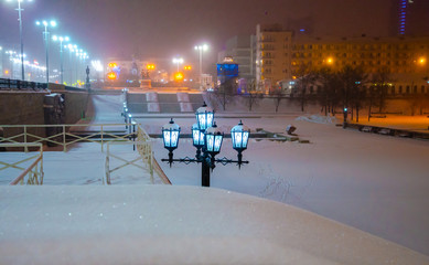 Pole with lanterns in the city on a winter night with snow and Blizzard.