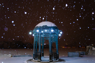An old metal gazebo on the shore of a frozen lake at night in winter.