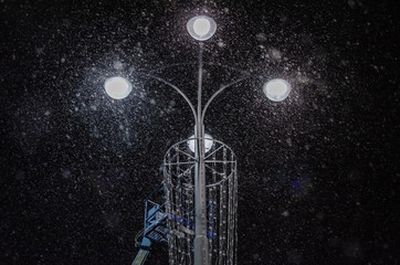 Pole with lanterns in the city on a winter night with snow and Blizzard.