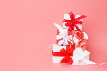 White gift boxes with red satin ribbons on a pink background. Festive presents for St. Valentine's Day, International Women's Day, wedding or engagement. Copy space.