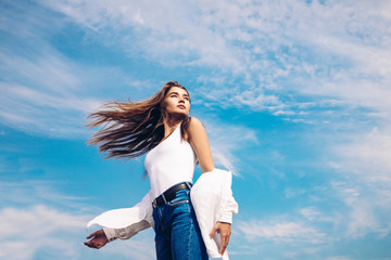 Fototapeta na wymiar Beautiful girl in a white shirt and blue jeans posing over the sky. Outdoor shot. Summer vacation concept.