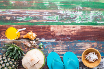 Orange juice pineapple coconut seashell and rubber sandals on color wood background, travel leisure concept.