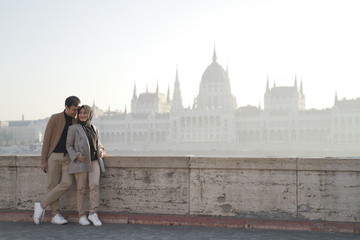 a couple posing against a river background and beautiful city buildings of budapest
