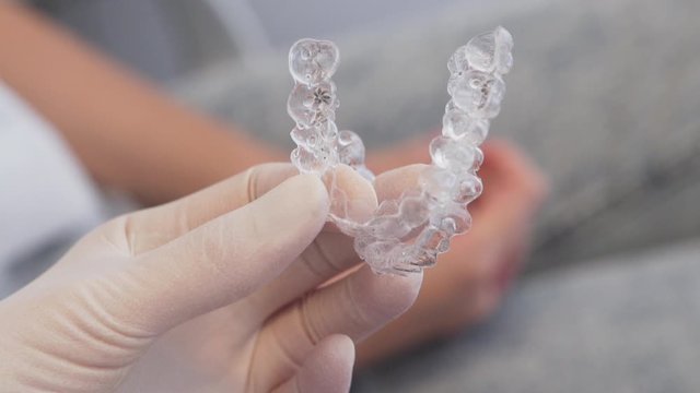 tight close-up of gloved hand holding two invisalign aligners, with patient in the background