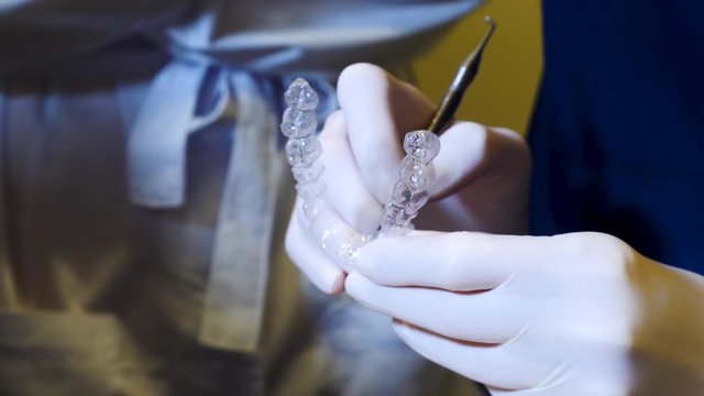 close-up of orthodontist handling an invisalign aligner, with doctor on the background