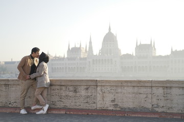 a romantic young couple posing against a river background and beautiful city buildings of budapest