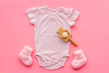 Pink bodysuit for baby girl near children's things on pink background top-down