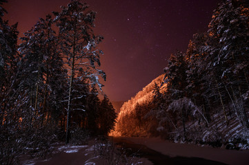 Winter landscape in the mountains. A frozen river flows, stars rotate in the sky.