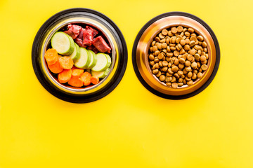 Healthy feed for cats and dogs. Bowls full of dry feed, meat and vegetables on yellow background top-down copy space