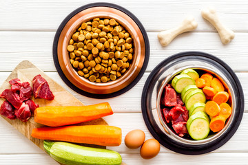 Ingredients of dry feed for dogs - meat, vegetables - near bones on white wooden background top-down