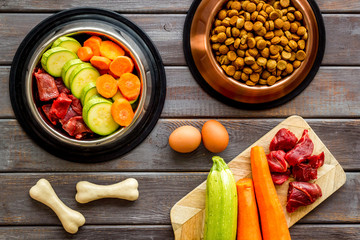 Ingredients of dry feed for dogs - meat, vegetables - near bones on dark wooden background top-down
