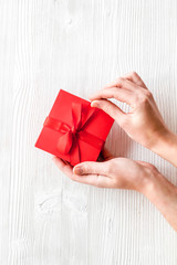 Unpack a gift on Valentine's Day. Women hand hold ribbon tied present box on white wooden background top-down copy space