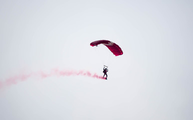 silhouette parachute stunt unfocused and blurry while gliding in the air with red smoke trail during an air exhibition