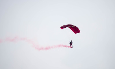silhouette parachute stunt unfocused and blurry while gliding in the air with red smoke trail during an air exhibition