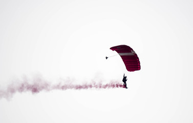 silhouette parachute stunt unfocused and blurry while gliding in the air with red smoke trail during an air exhibition