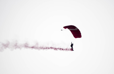 silhouette parachute stunt unfocused and blurry while gliding in the air with red smoke trail during an air exhibition