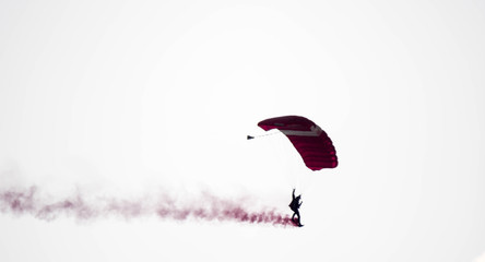 silhouette parachute stunt unfocused and blurry while gliding in the air with red smoke trail during an air exhibition
