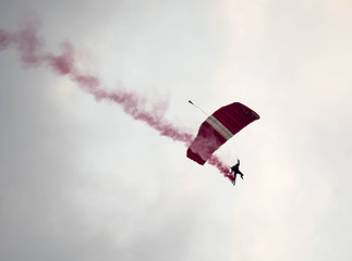 silhouette parachute stunt unfocused and blurry while gliding in the air with red smoke trail during an air exhibition
