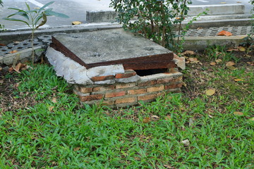 Closeup and focus on broken brick wall with hole of a drain on green grass field