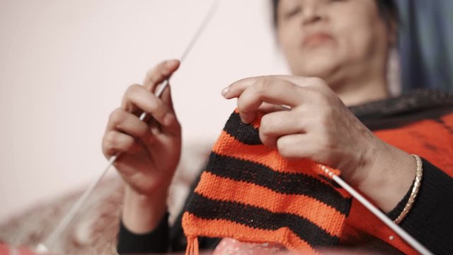 Traditional Indian woman watching hew knit and continues knitting with black and red thread. 4k footage of knit work tie-up hand work
