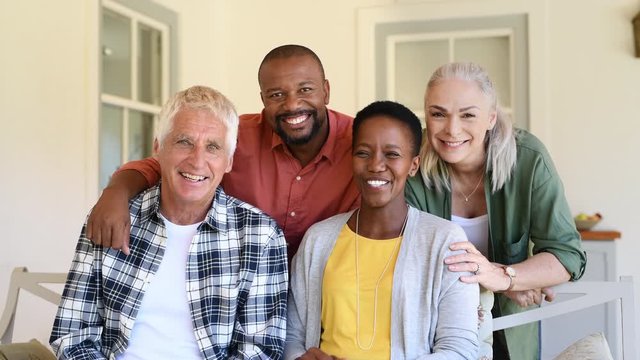 Senior couple with mature man and african woman posing for a photo sitting at courtyard. Portrait of happy multiethnic people sitting on couch under patio. Cheerful men and women looking at camera.