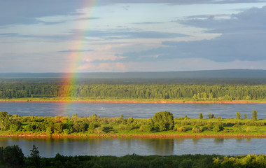 Rainbow over the river and forest. Bright rainbow.