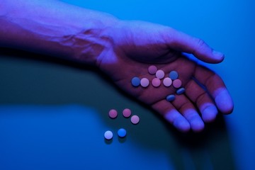 Man's hand with pills. Blue light. The concept of suicide, drug overdose, drug addiction, loss of consciousness. Danger of death. Copy space.