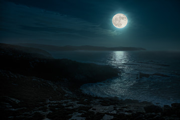 A beautiful full moon night on the Atlantic. The place is in the north of Spain in Galicia and is called Cape Punta Nariga. The moon illuminates the wild sea and the light is reflected from the water. © wewi-creative