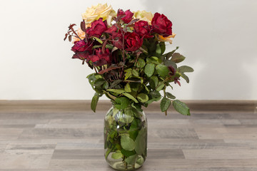 Roses flowers in a glass jar on the floor against a white wall