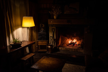 Interior of a wooden cozy and relaxing cabin with comfortable couches, country decoration, dimly lit by the fireplace and lamp. Concept of silence, tranquility, time to rest and relaxation.