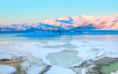 Beautiful winter lanscape with cracks on the surface of the turquoise (green) ice next to snowy mountains - Fjord and Frozen lake, Norway