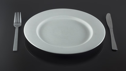 empty white plate with knife and fork on a shiny surface