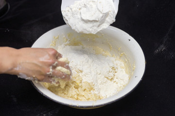 Hands of the cook prepare the dough for bread on a black background. Restrained shot with flour.