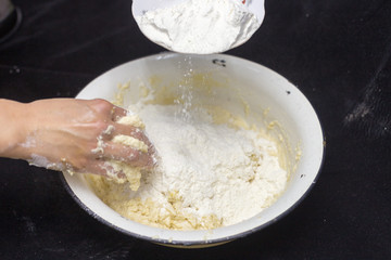 Hands of the cook prepare the dough for bread on a black background. Restrained shot with flour.