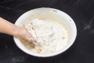 Hands of the cook prepare the dough for bread on a black background. Restrained shot with flour.