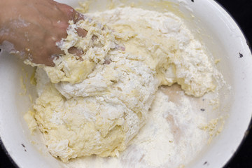 Hands of the cook prepare the dough for bread on a black background. Restrained shot with flour.