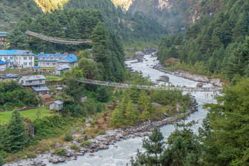 Group of trekker walking on hanging bridge for crossing Dudh Kosi river nearly Phakding village (2600 metres) the main stopping point for trekkers on their way to Everest base camp, Nepal. - obrazy, fototapety, plakaty