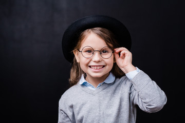 Pretty little girl looking at you with toothy smile while touching eyeglasses