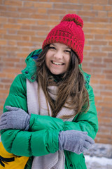 Woman hipster in bright clothes laughing and smiling. Young happy girl in a red knit hat, green jacket, grey scarf, yellow small bag. Women's fashion.