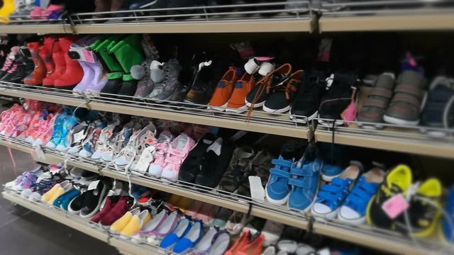 The shelf with footwear for boys, girls and children in the store. Kids shoes, sneakers and various colored boots in shopping mall or hypermarket