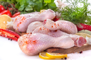 Fresh chicken legs with tomatoes, lemon and spices, on a white background