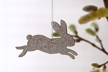Fototapeta premium Easter time. Easter rabbit silver decoration on willow twigs on a white background. Easter concept. Spring religious holiday background.