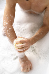 Overview of shirtless young man with sponge washing his arms with foam
